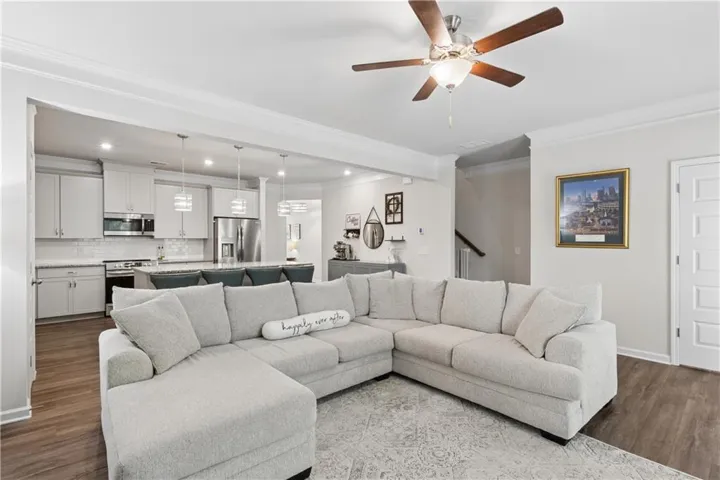 Open-concept living area featuring wood-finish flooring, a ceiling fan, and crown molding