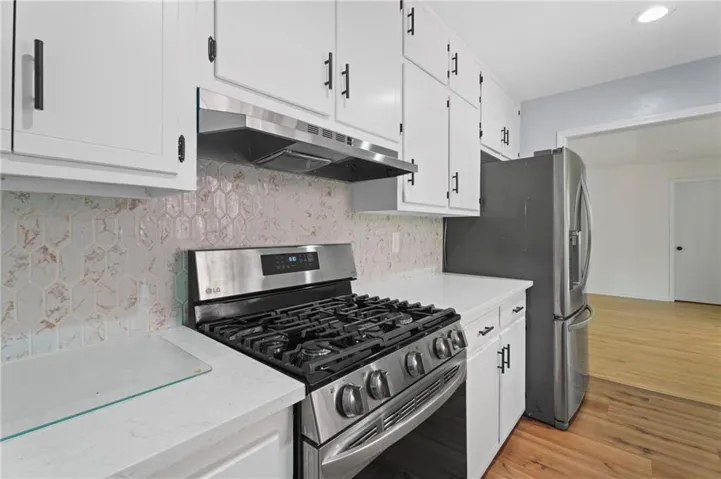 Kitchen featuring white cabinetry with black hardware, white countertops, and a full stainless steel appliance suite including a gas range and refrigerator