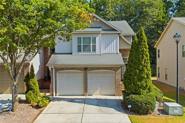 Brick and siding exterior with a two-car garage, concrete driveway, and mature landscaping