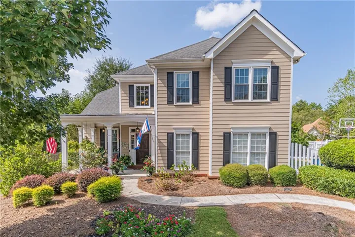 Traditional-style exterior with neutral siding, black window shutters, a covered porch with white columns, and a front walkway