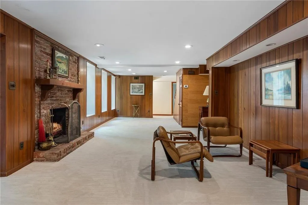 Living room featuring wood walls, a brick fireplace, and light colored carpet