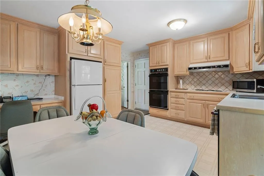Kitchen featuring light brown cabinetry, hanging light fixtures, white fridge, and black double oven
