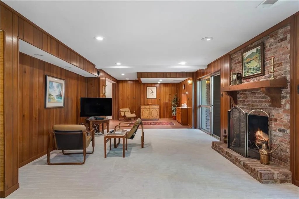 Carpeted basement living room with a fireplace and wood walls