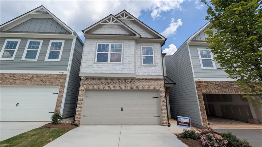 Light-toned siding exterior with brick accents, featuring a two-car garage and a paved driveway