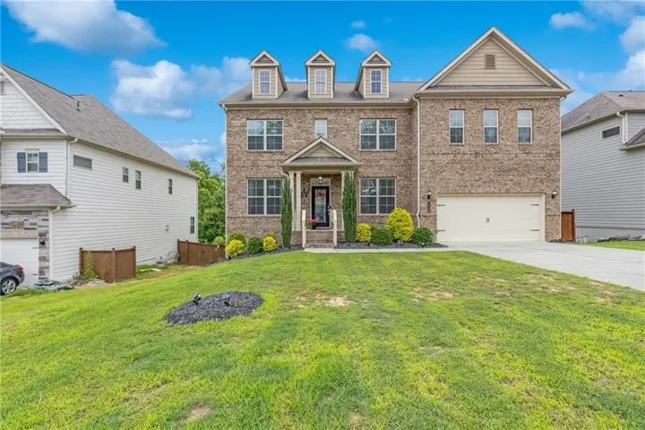 Brick facade home featuring a prominent two-car garage, multiple dormer windows, and a covered front entry