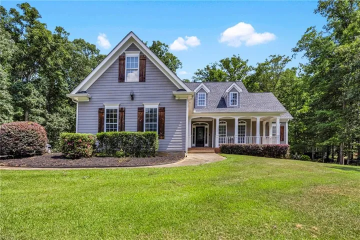 Gray siding exterior with dormer windows, a covered front porch, decorative shutters, and mature landscaping