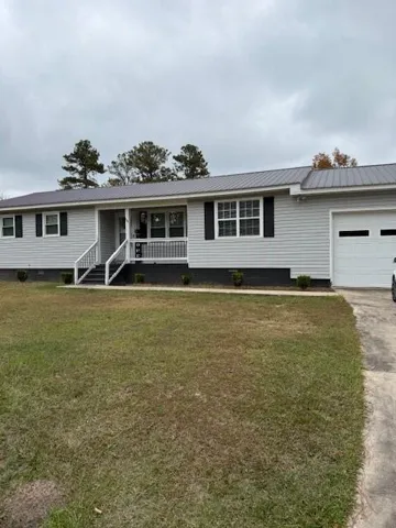 Ranch-style home with a garage, covered porch, a metal roof, driveway, and a front yard