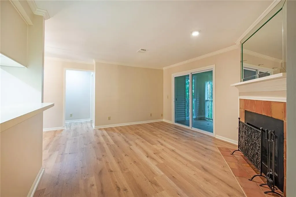 Living room featuring crown molding, brand new light laminate wood-style floors, and a tiled fireplace with mantle