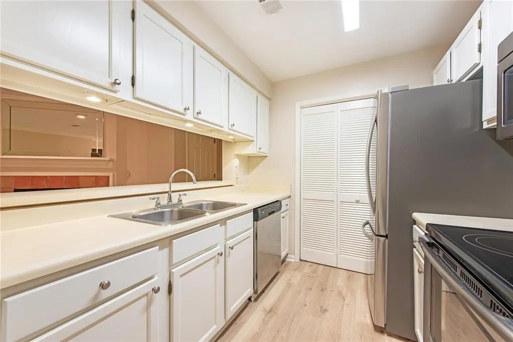 Kitchen featuring white cabinets, appliances with stainless steel finishes, light wood-type flooring, and sink