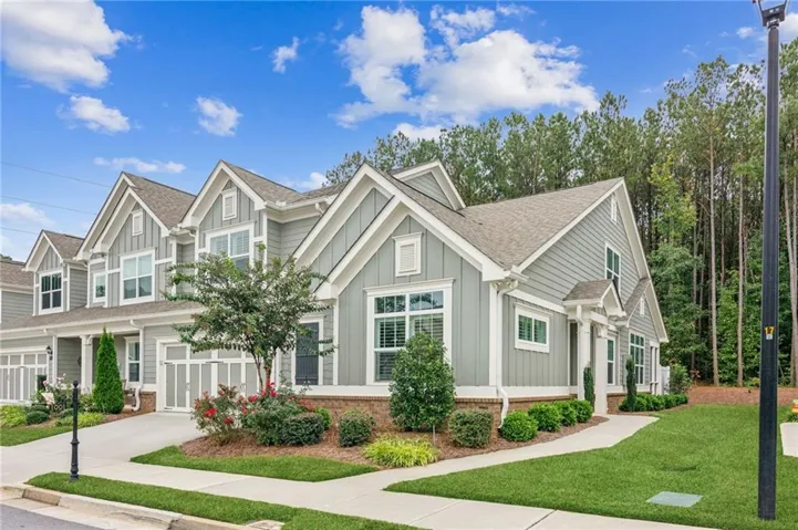 Contemporary townhome featuring light gray siding, white trim, multiple gables, an attached garage, and manicured landscaping