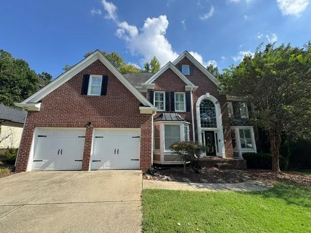 Brick exterior with white garage doors, a decorative arched window, a bay window, and a gabled roofline