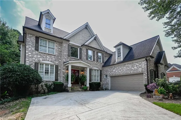 Traditional-style residence featuring a multi-gabled roofline, light-colored brick facade, and a covered portico entrance