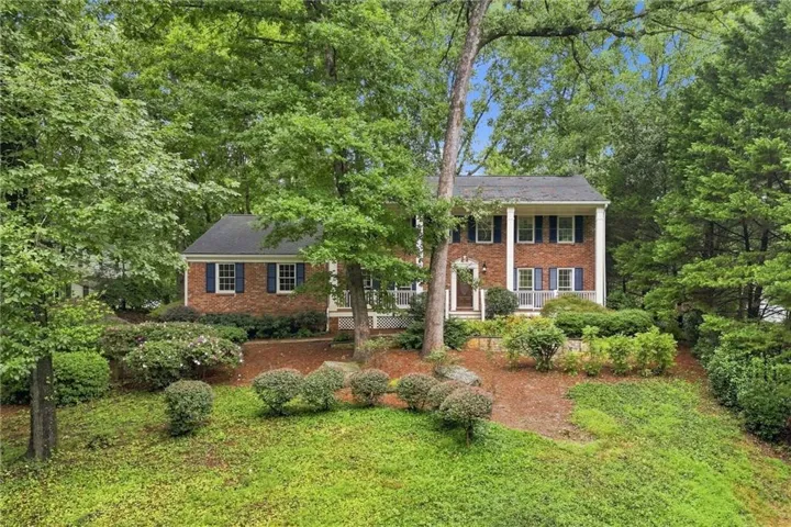 Brick exterior with white columns, dark blue window shutters, a covered entry, and mature landscaping