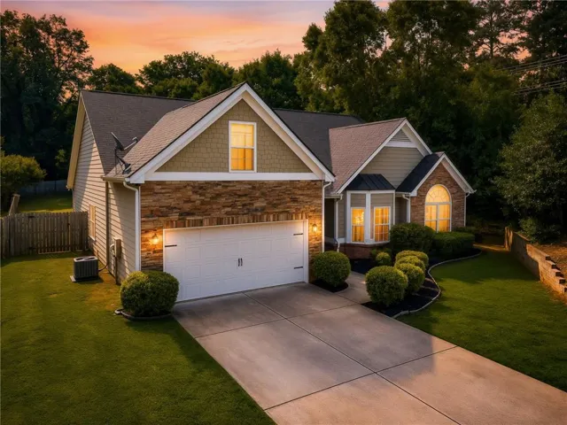 Exterior featuring stone accents and siding, a two-car garage, established landscaping, and a concrete driveway