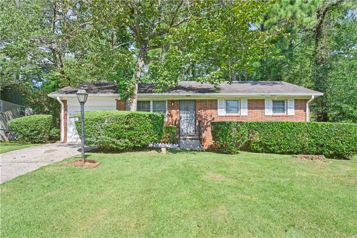 Brick facade residence featuring a front lawn, mature trees, an attached garage, and a concrete driveway