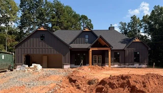 Board and batten siding with dark trim accents, covered entry with wood posts, dual entry doors, and an attached garage