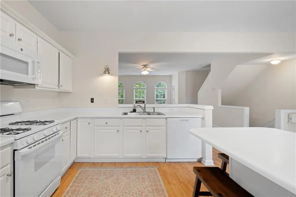 Kitchen featuring white appliances, light wood-type flooring, ceiling fan, a peninsula, and white cabinetry