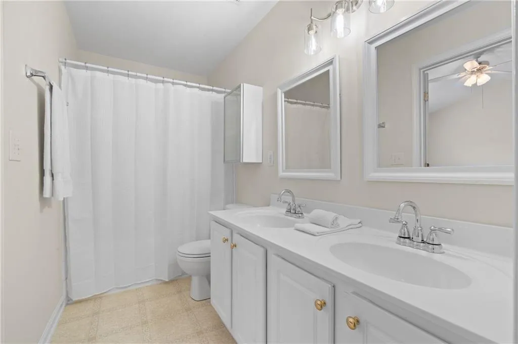 Full bath with double vanity, a shower with curtain, tile patterned floors, and a ceiling fan