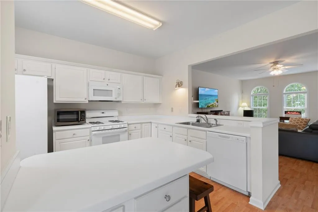 Kitchen with open floor plan, a peninsula, white appliances, light wood-style floors, and light countertops