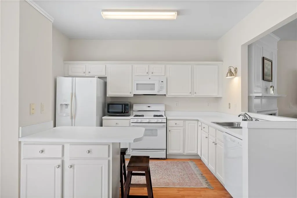 Kitchen featuring a peninsula, white appliances, light wood-style flooring, white cabinetry, and light countertops
