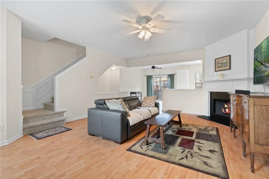 Living area featuring a ceiling fan, stairs, light wood finished floors, and a warm lit fireplace