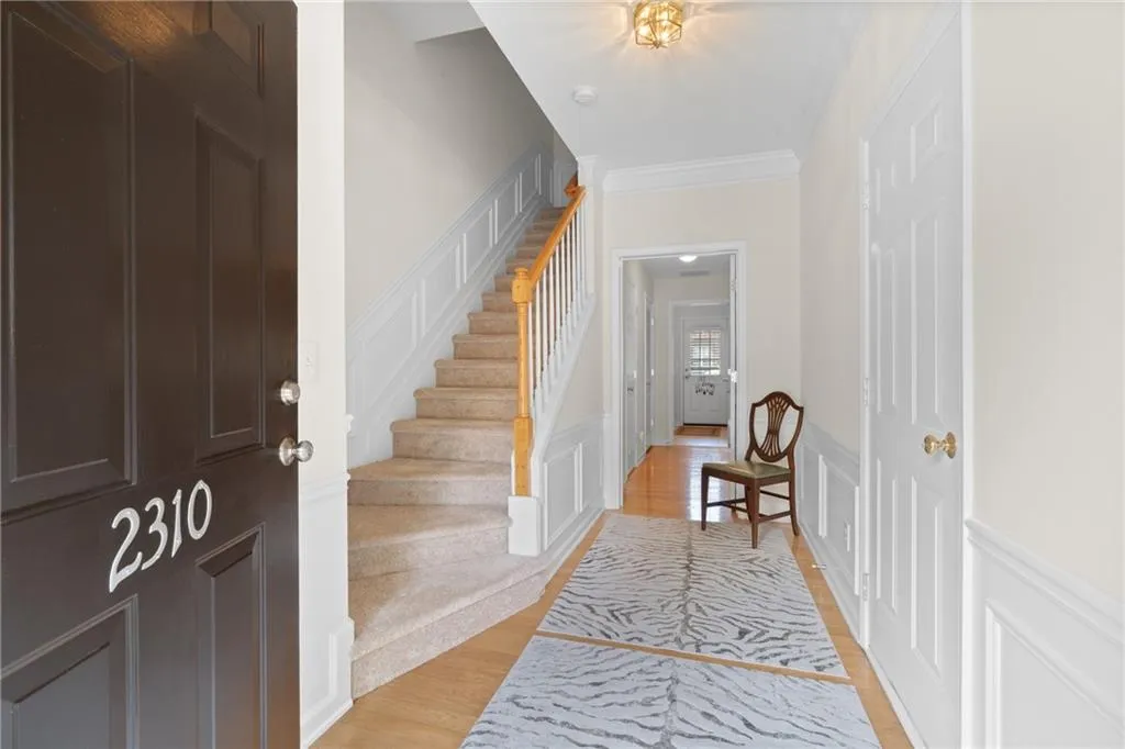 Entrance foyer with a decorative wall, wainscoting, stairs, light wood-style floors, and crown molding
