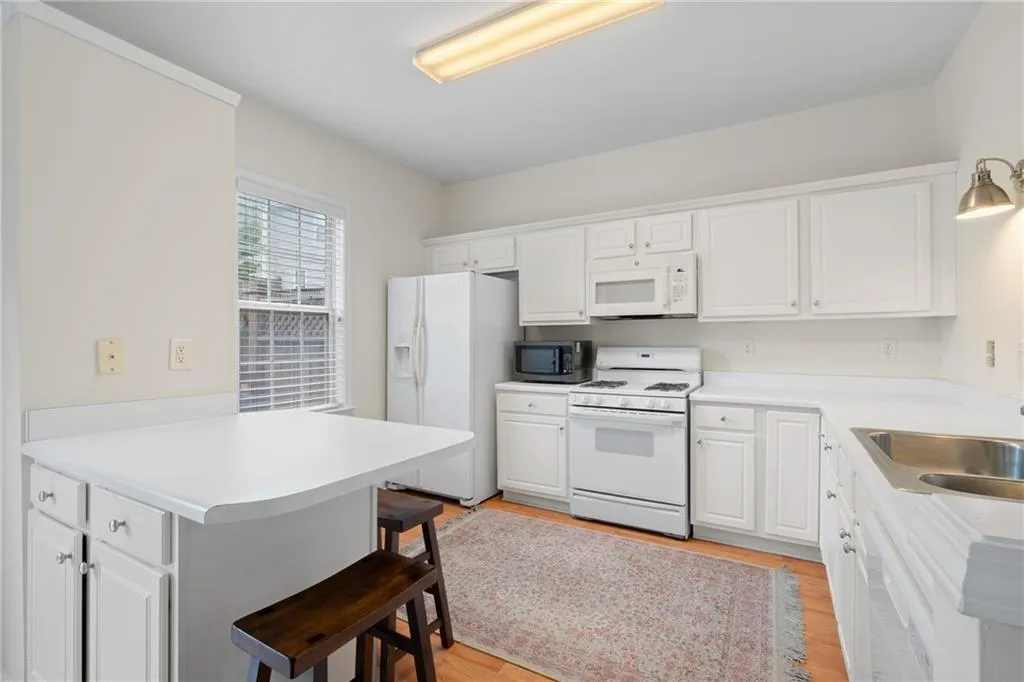Kitchen with white appliances, a peninsula, a kitchen bar, light wood-type flooring, and white cabinets