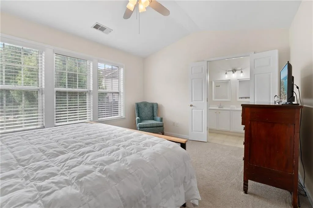 Bedroom featuring light colored carpet, vaulted ceiling, connected bathroom, and ceiling fan