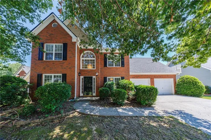 Brick exterior with gabled roofline, arched window, two-car garage, and established landscaping