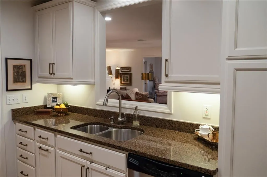 Kitchen featuring dark stone countertops, dishwasher, white cabinetry, and sink