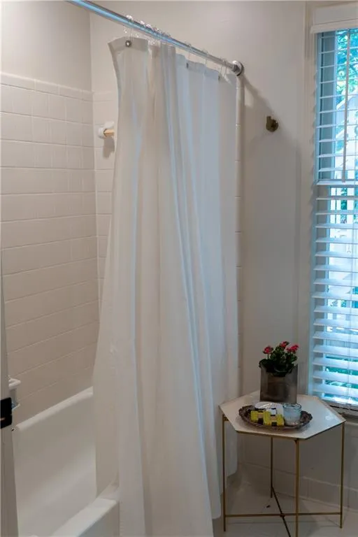 Bathroom featuring shower / tub combo and tile patterned floors, new toilet and headknocker cabinetry.