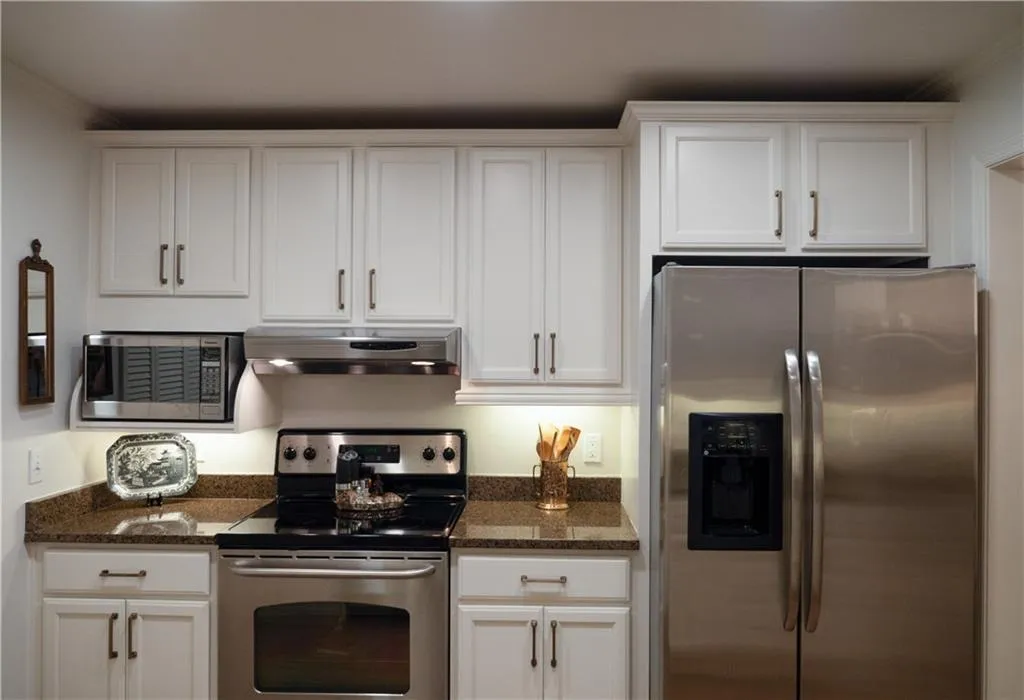 Kitchen featuring dark stone counters, ornamental molding, appliances with stainless steel finishes, and white cabinets