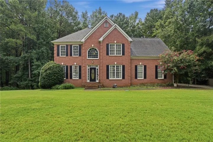 Brick exterior, gabled roofline, arched window above the entry, black shutters, and a prominent front door