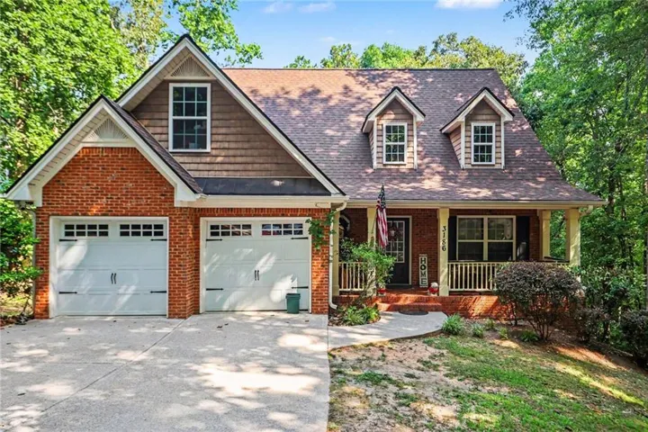 Traditional-style exterior featuring brick and shingle siding, a two-car garage with white doors, a covered front porch with white railings and pillars, and a concrete driveway