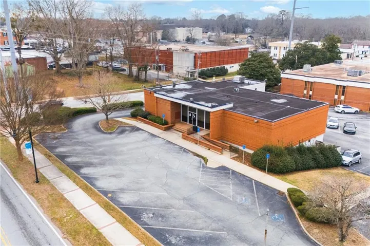 Brick exterior building with a flat roof, featuring a paved parking lot, a curved entrance driveway, and established landscaping