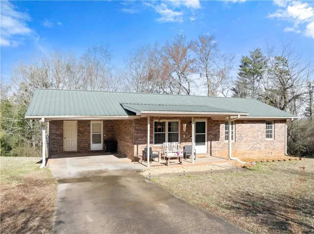 Ranch-style home featuring an attached carport, a porch, concrete driveway, a metal roof, and brick siding