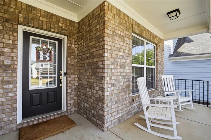 Inviting covered front porch with brick exterior, white trim details, and a black front door with a glass insert