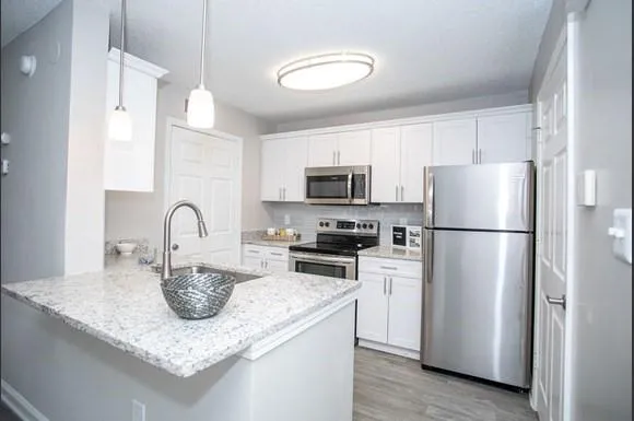 Kitchen featuring kitchen peninsula, white cabinetry, pendant lighting, and stainless steel appliances