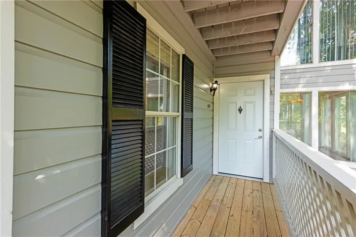 Exterior entry featuring light grey siding, black louvered shutters, a white entry door, and wood-finish flooring on the porch