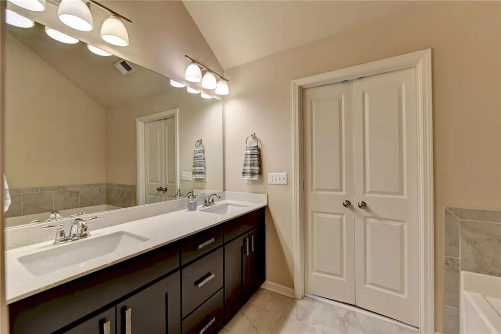Bathroom featuring lofted ceiling, dual sinks, large vanity, tile flooring, and a bathing tub