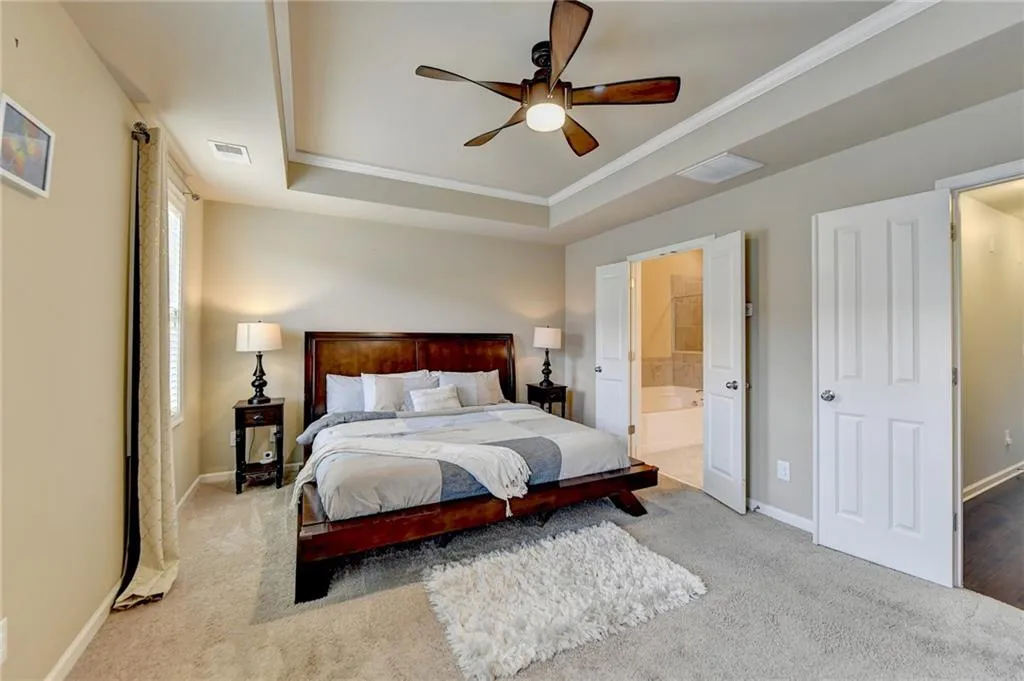 Carpeted bedroom featuring a raised ceiling, connected bathroom, crown molding, and ceiling fan