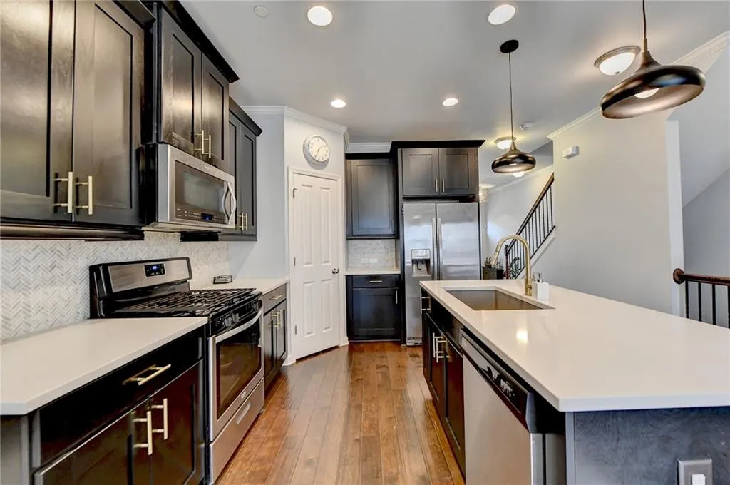 Kitchen with appliances with stainless steel finishes, ornamental molding, a kitchen island with sink, light hardwood / wood-style floors, and pendant lighting