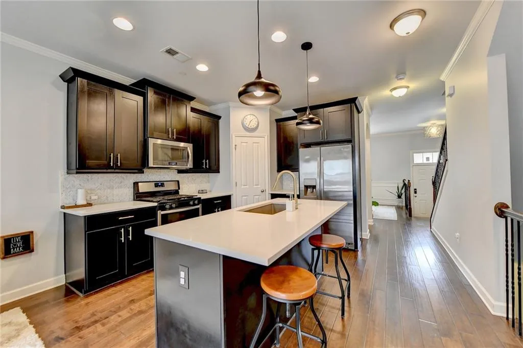 Kitchen with sink, an island with sink, appliances with stainless steel finishes, backsplash, and pendant lighting