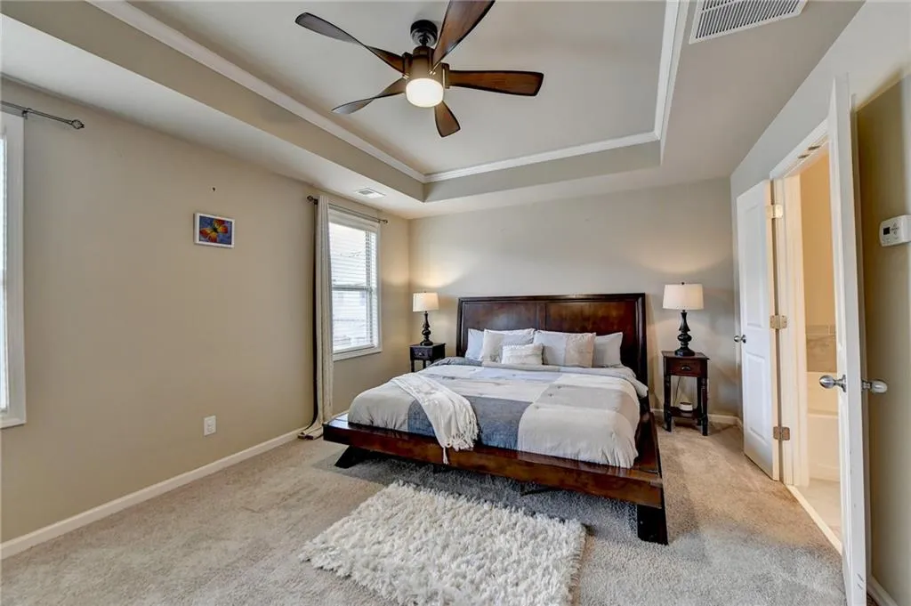 Bedroom featuring light colored carpet, ceiling fan, and a raised ceiling