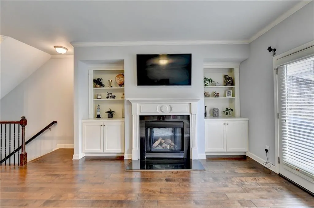 Living room featuring wood-type flooring, built in features, and crown molding
