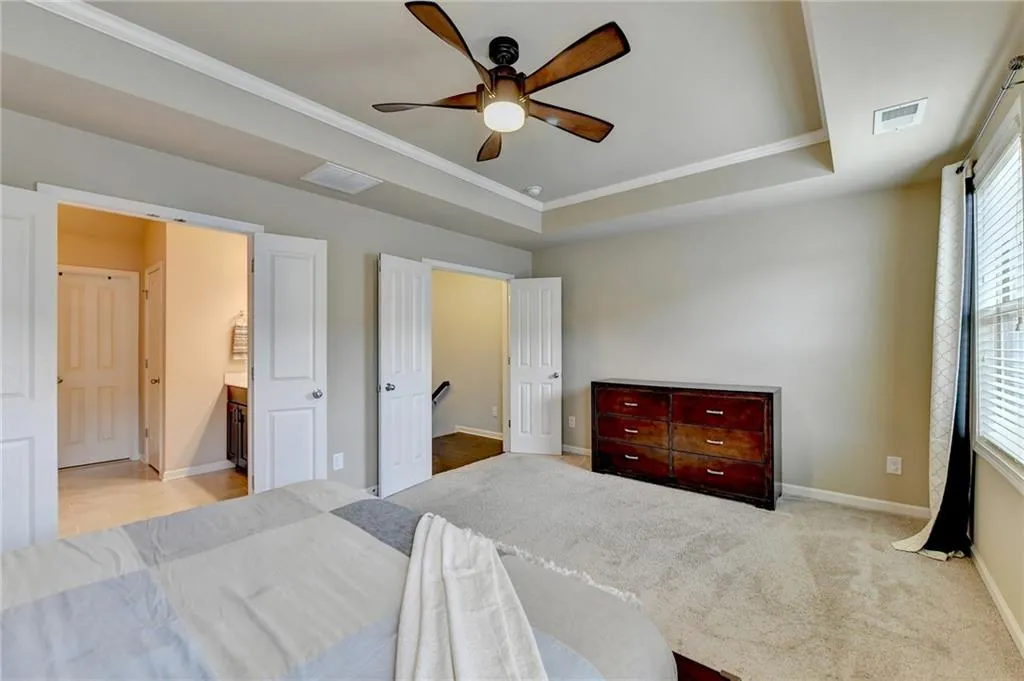 Bedroom featuring ornamental molding, light carpet, ceiling fan, and a raised ceiling