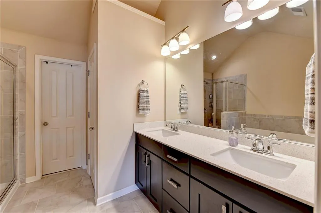 Bathroom with dual sinks, vaulted ceiling, vanity with extensive cabinet space, shower with separate bathtub, and tile flooring