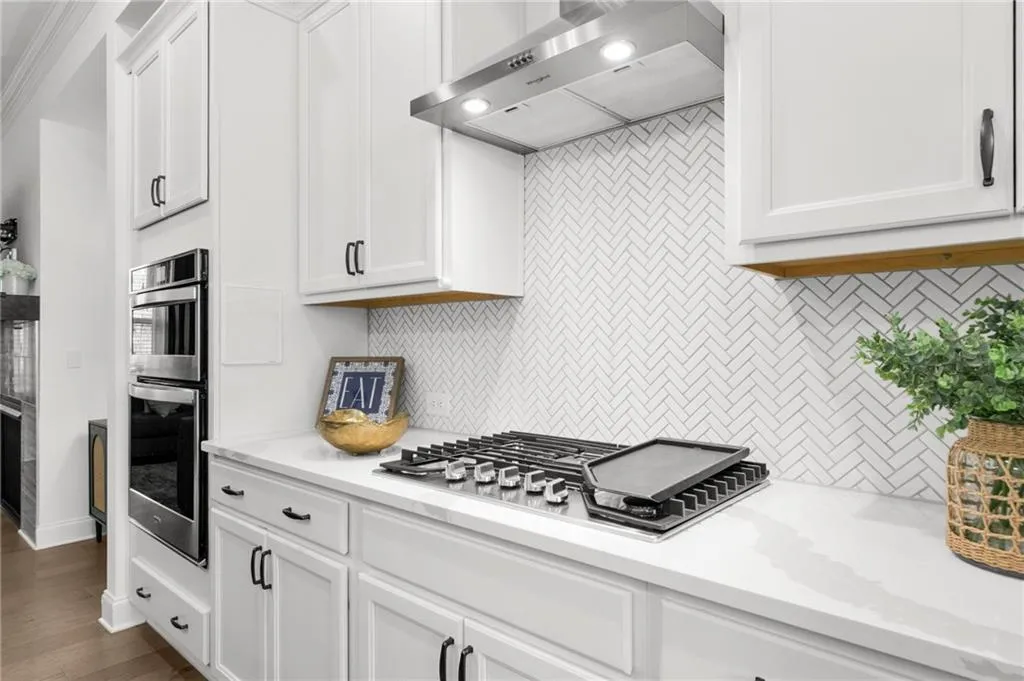 Kitchen with extractor fan, white cabinetry, backsplash, light stone counters, and stainless steel appliances