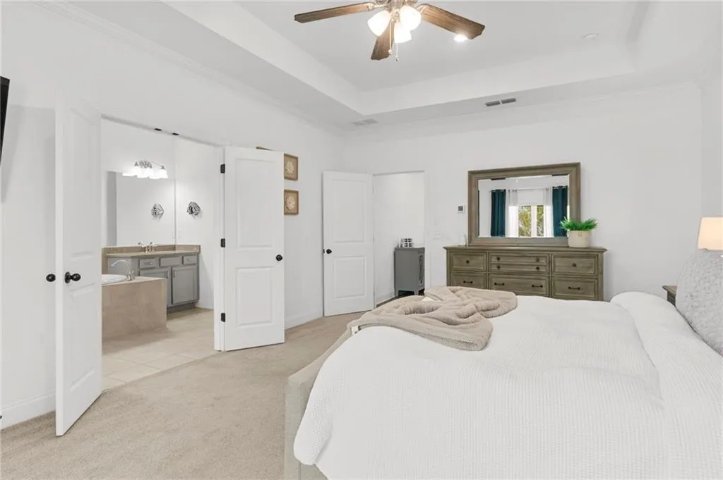 Bedroom featuring light colored carpet, a raised ceiling, ornamental molding, and ceiling fan