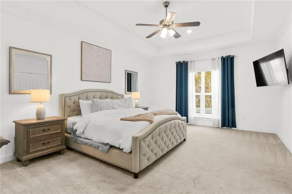 Bedroom with light colored carpet, a ceiling fan, and a raised ceiling